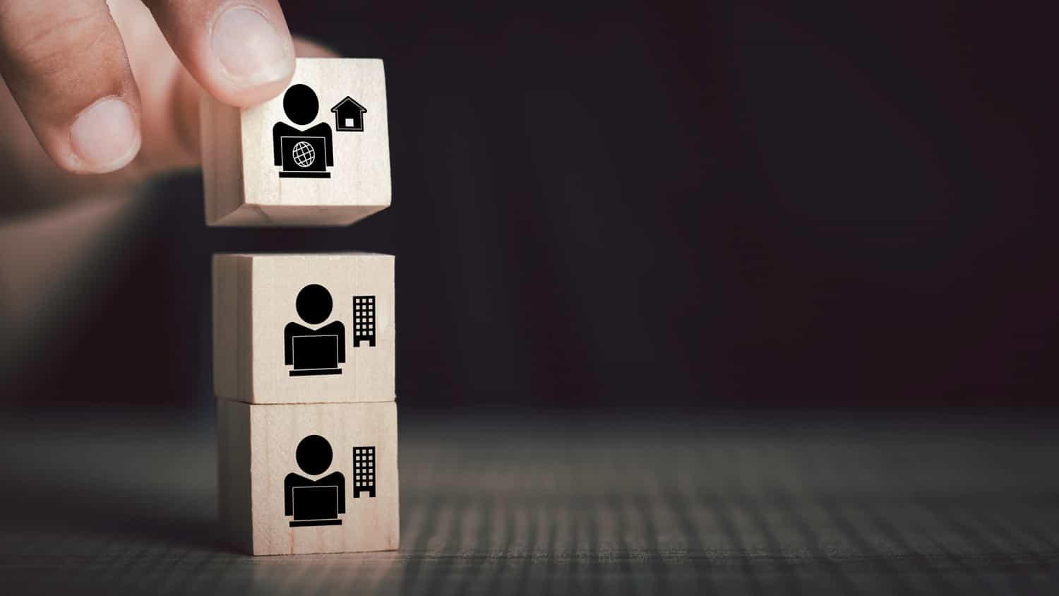 Wooden blocks are stacked to show options for hybrid workplace, teamwork, outsourcing and in-house options.