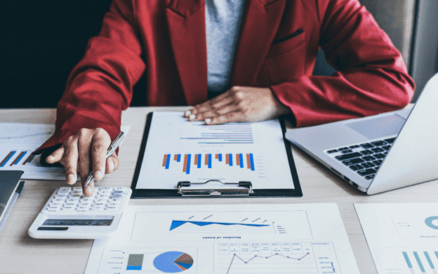Person sitting by a laptop reviewing a bunch of charts and graphs printed on paper.